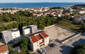 Oversigtsbillede af et kystnært boligområde med bygninger, en parkeringsplads og en strand.