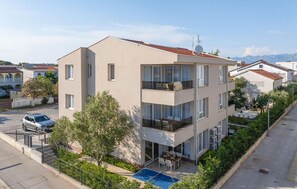 A multi-story building with balconies, a swimming pool, and a car parked in front. - Apartment in Vir (475) (Vir)