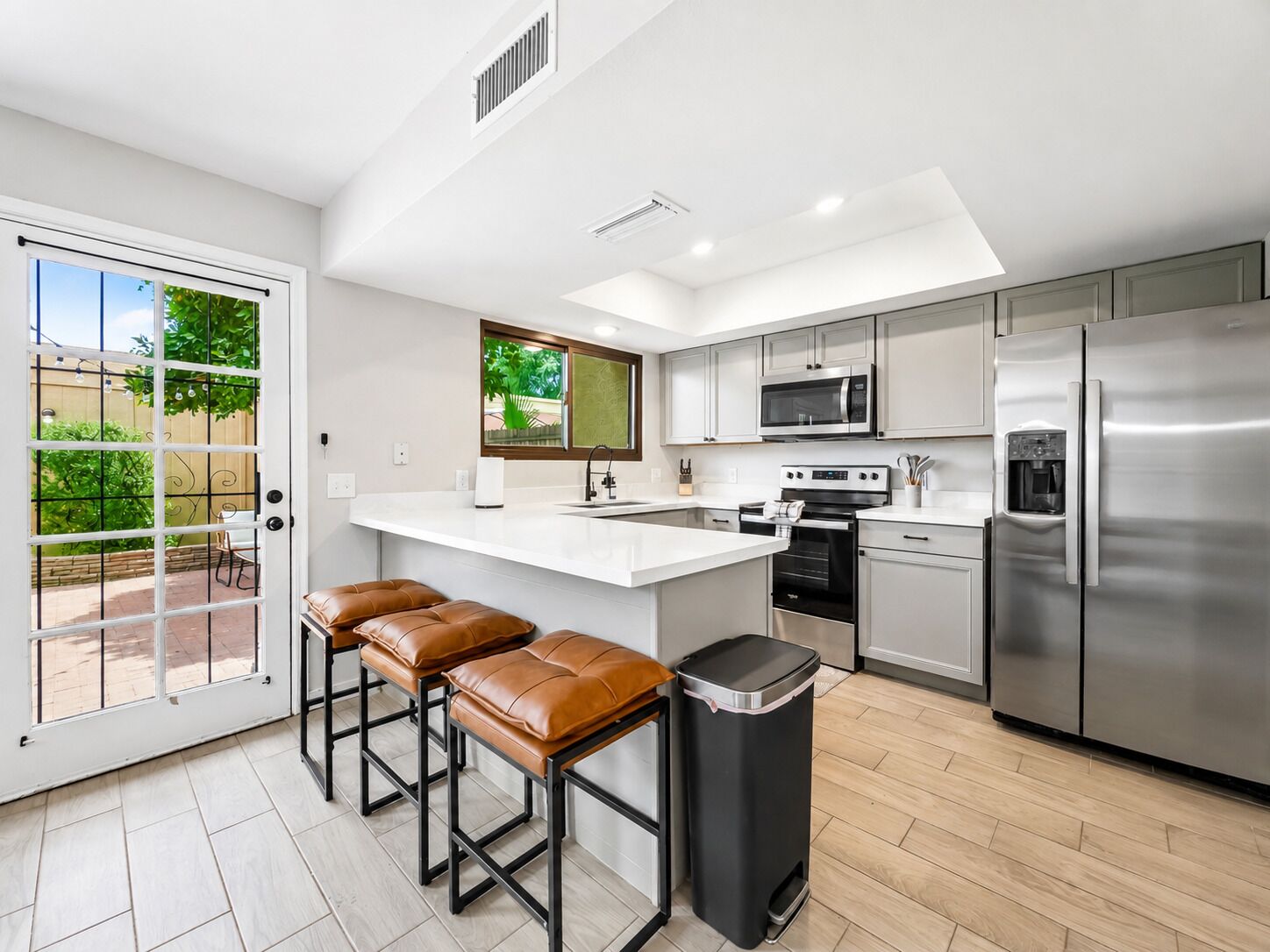 A modern kitchen with a central island, stainless steel appliances, and a view to the outside.