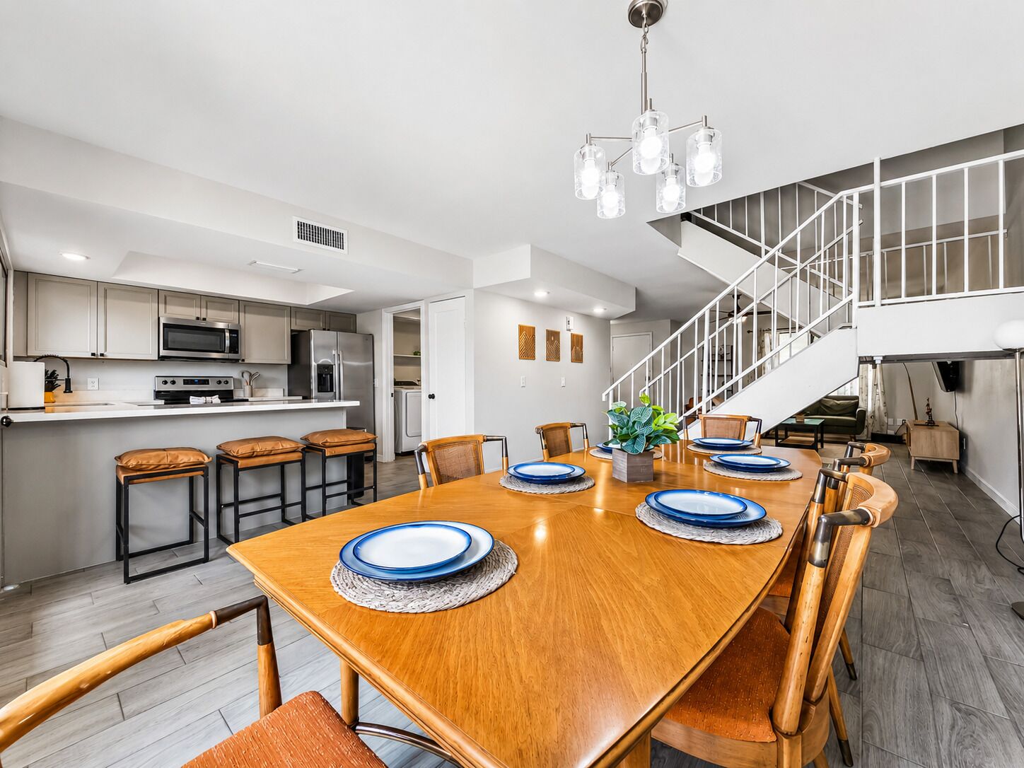 A modern kitchen with stainless steel appliances, a dining area with a wooden table and chairs, and a staircase leading to an upper level.