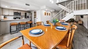 Une cuisine moderne équipée d’appareils électroménagers en acier inoxydable, un coin repas avec une table et des chaises en bois, et un escalier menant à l’étage supérieur.