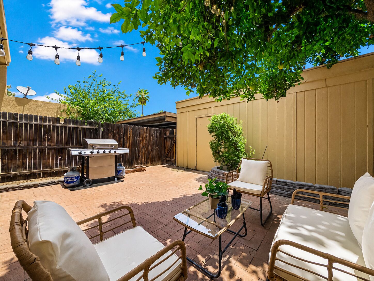 A backyard patio with outdoor furniture, a barbecue grill, and string lights.
