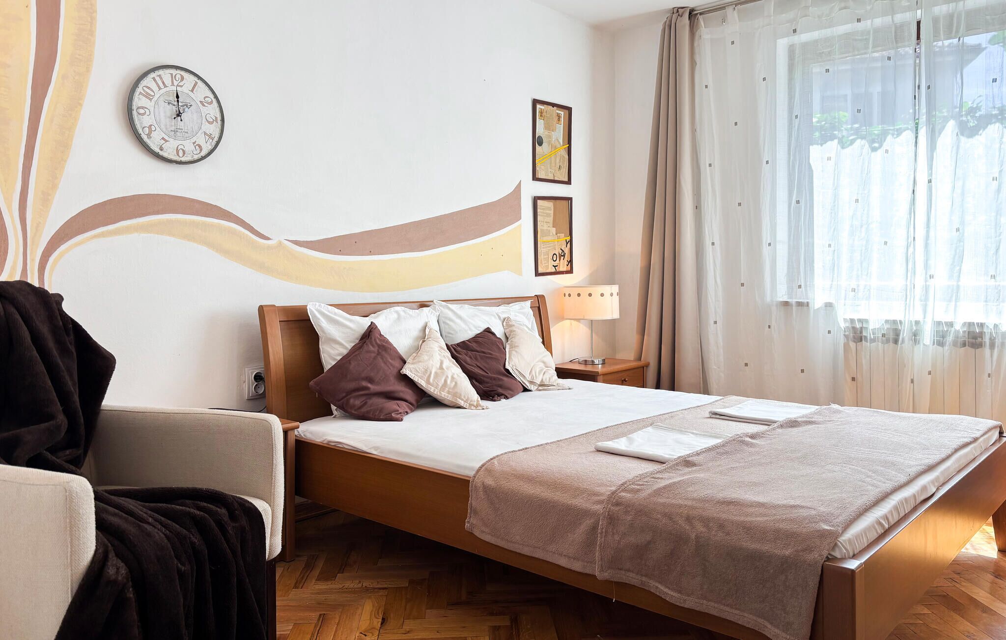A bedroom with a wooden bed, a clock, a lamp, and a window with curtains.