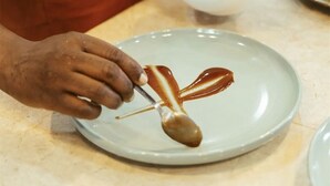 A person in a kitchen preparing food, with a bowl of sauce and a plate with sauce on a countertop.