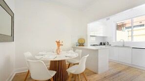 Une cuisine moderne avec des meubles blancs, une table de salle à manger ronde entourée de chaises blanches et une grande fenêtre.