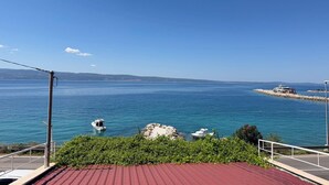 Vista costeira com céu claro, mar calmo e um afloramento rochoso.