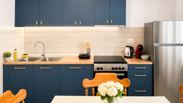 Una cocina moderna con armarios azul oscuro, un lavamanos de acero inoxidable, una estufa a gas y un refrigerador.