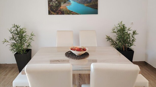 Una mesa de comedor con un tazón de bocadillos, dos plantas en macetas y un cuadro de paisaje colgado en la pared.