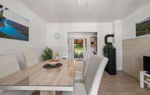 A modern dining area with a wooden table, white chairs, and a view of a garden through an open door. - Gorgeous home in Razvode (Razvode)