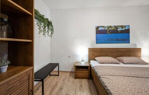 Ein Schlafzimmer mit einem hölzernen Kopfteil, einem Bett mit gemusterten Betttextilien, einem Nachttisch mit Lampe, einer Bank und einer Wandpflanze.