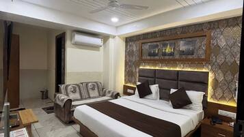 A modern hotel room with a large bed, a sofa, a desk, and a ceiling fan.