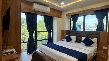 A hotel room with a bed, a desk, a chair, an air conditioner, and a ceiling fan.