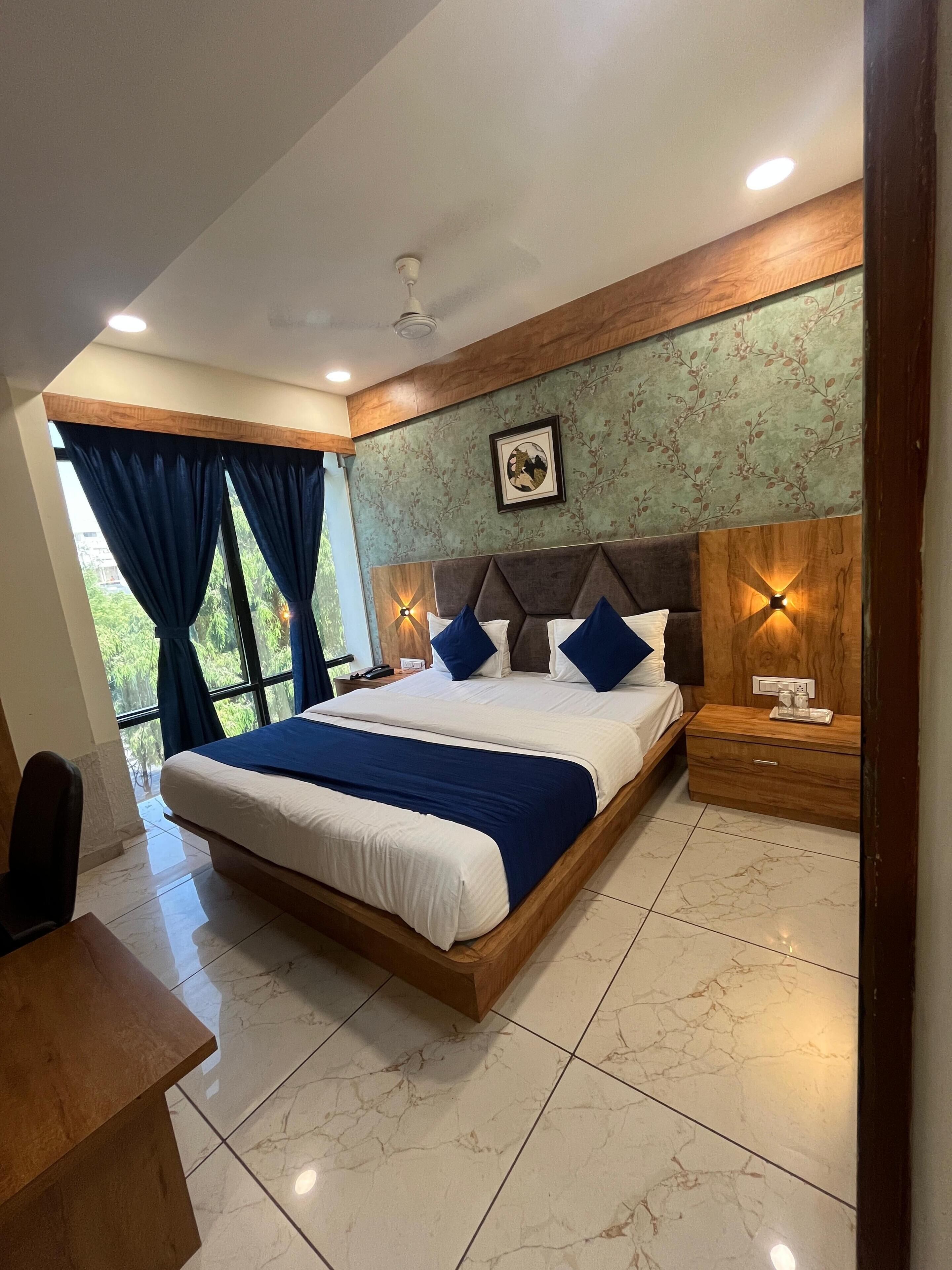 A bedroom with a large bed, a nightstand, a desk, and a window with curtains.