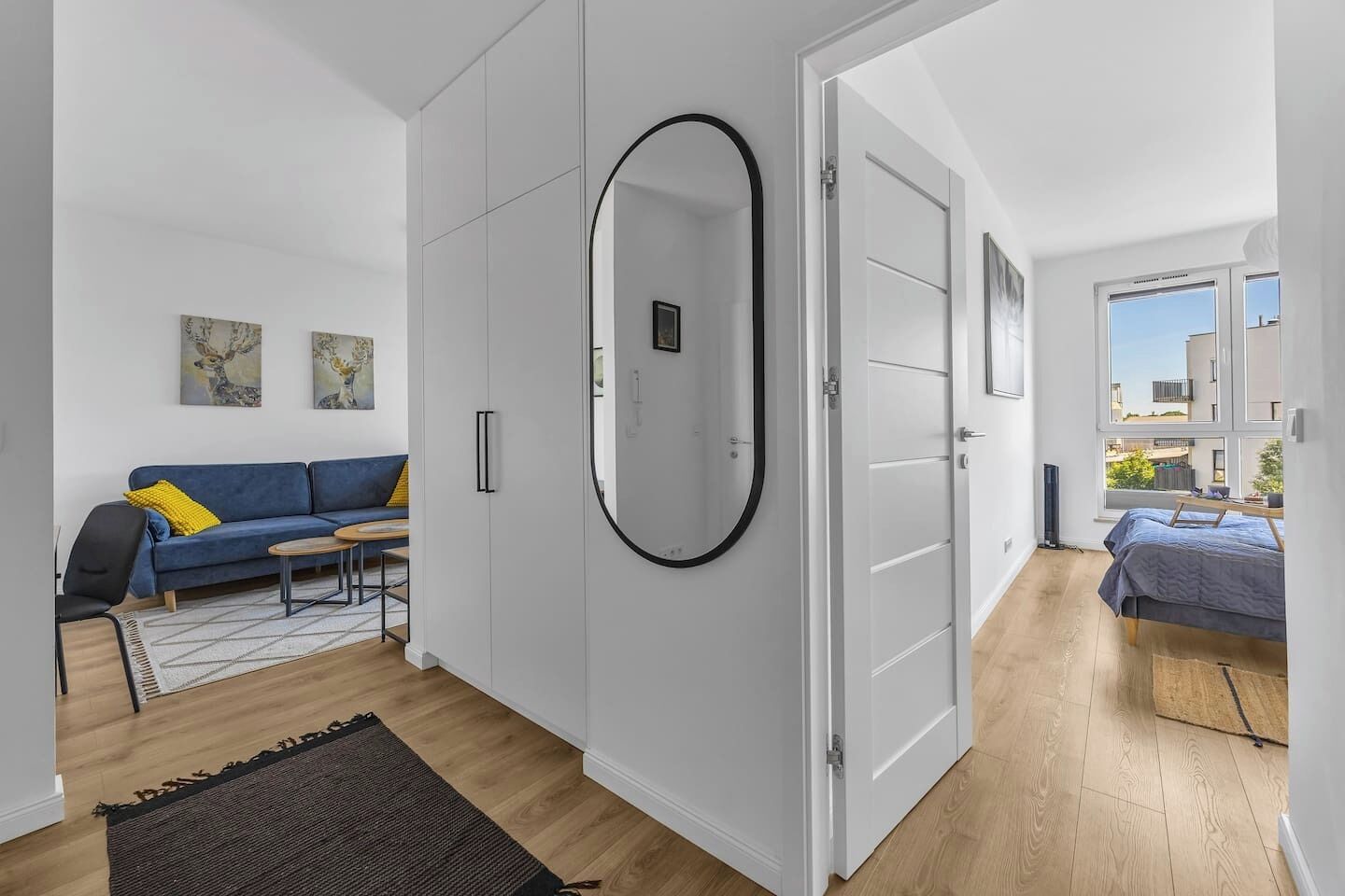 A modern apartment with a sofa, a dining table, a large mirror, and a bed.