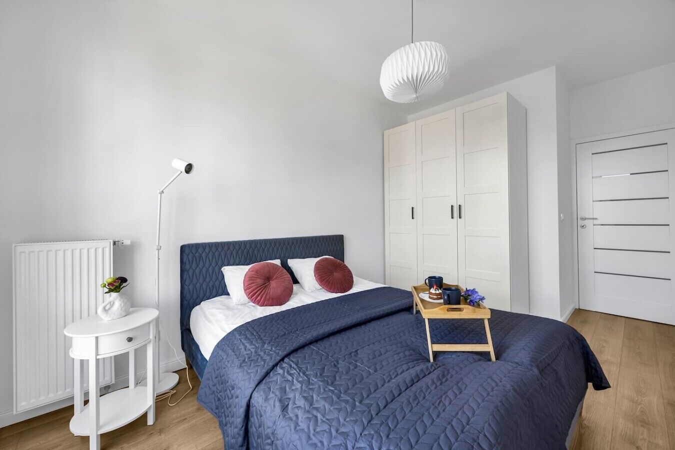 A bedroom with a bed, bedside table, radiator, wardrobe, and a hanging light fixture.