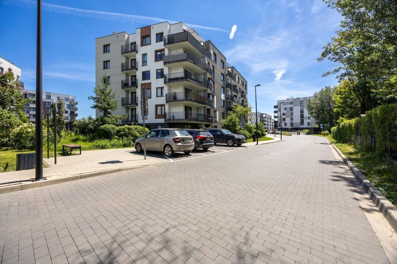 A multi-story residential building with balconies, a paved street, and parked cars.