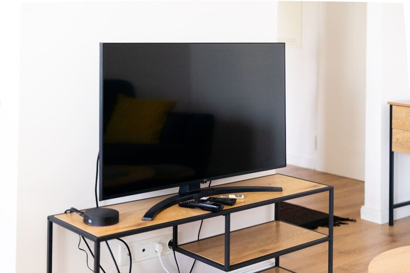 A television on a wooden TV stand with a remote control, a power outlet, and a cable management system.