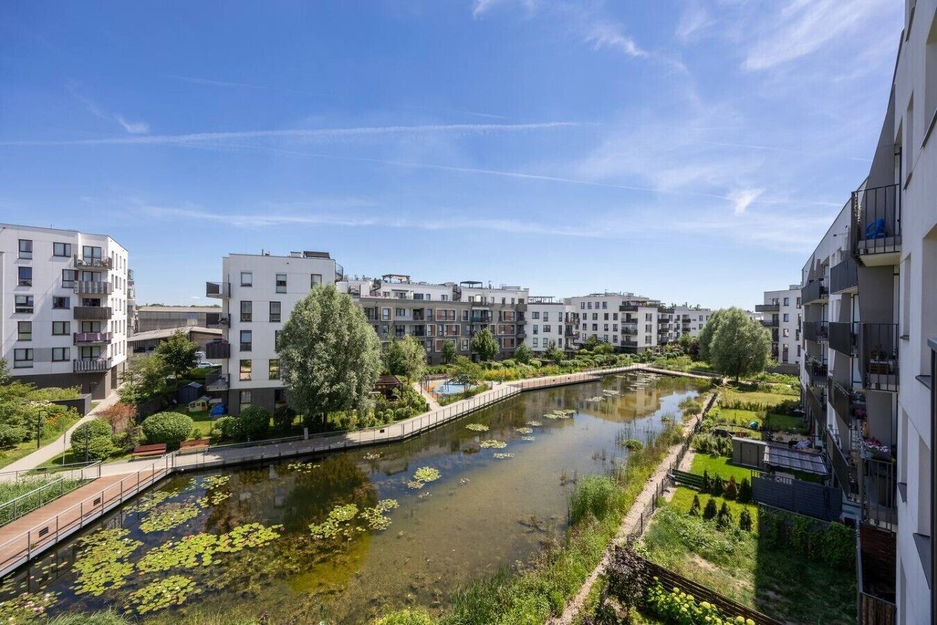 Zona residencial com edifícios de apartamentos modernos, um canal com nenúfares e um céu azul límpido.