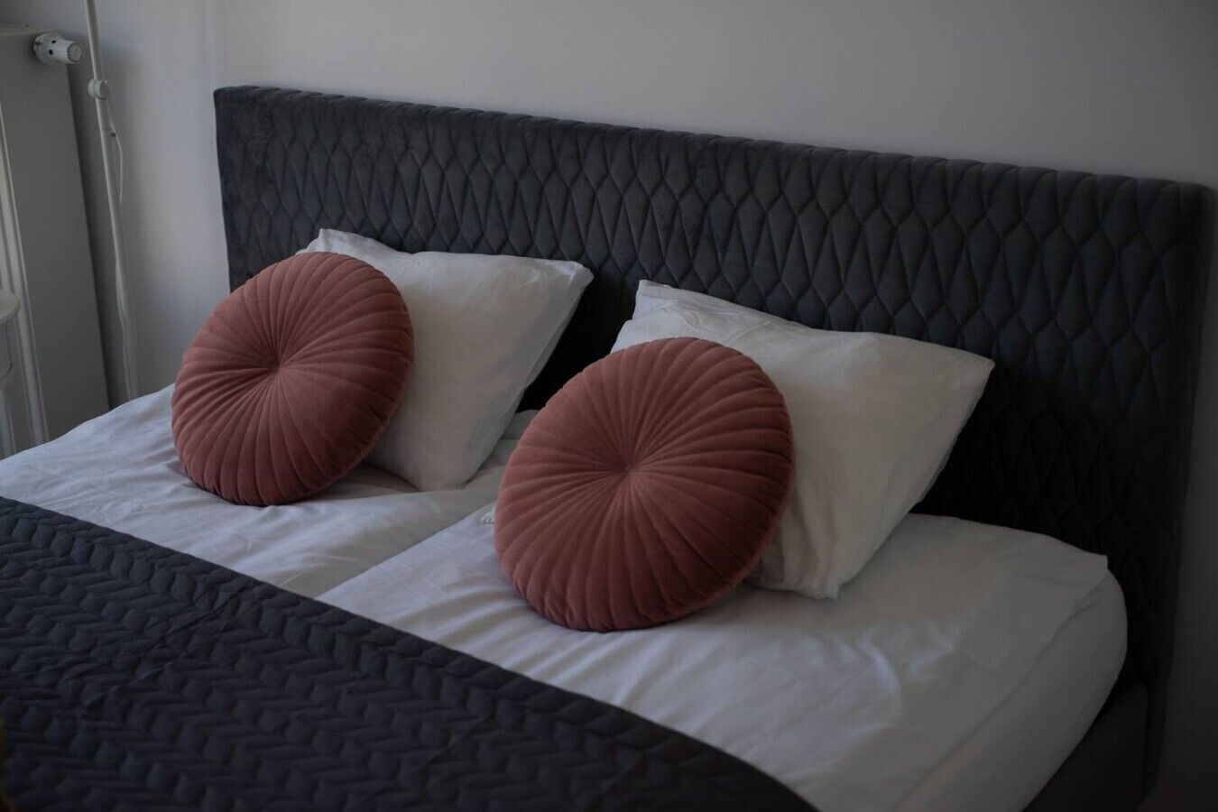 A bed with a black headboard, two white pillows, and two round, ribbed, pink accent pillows.