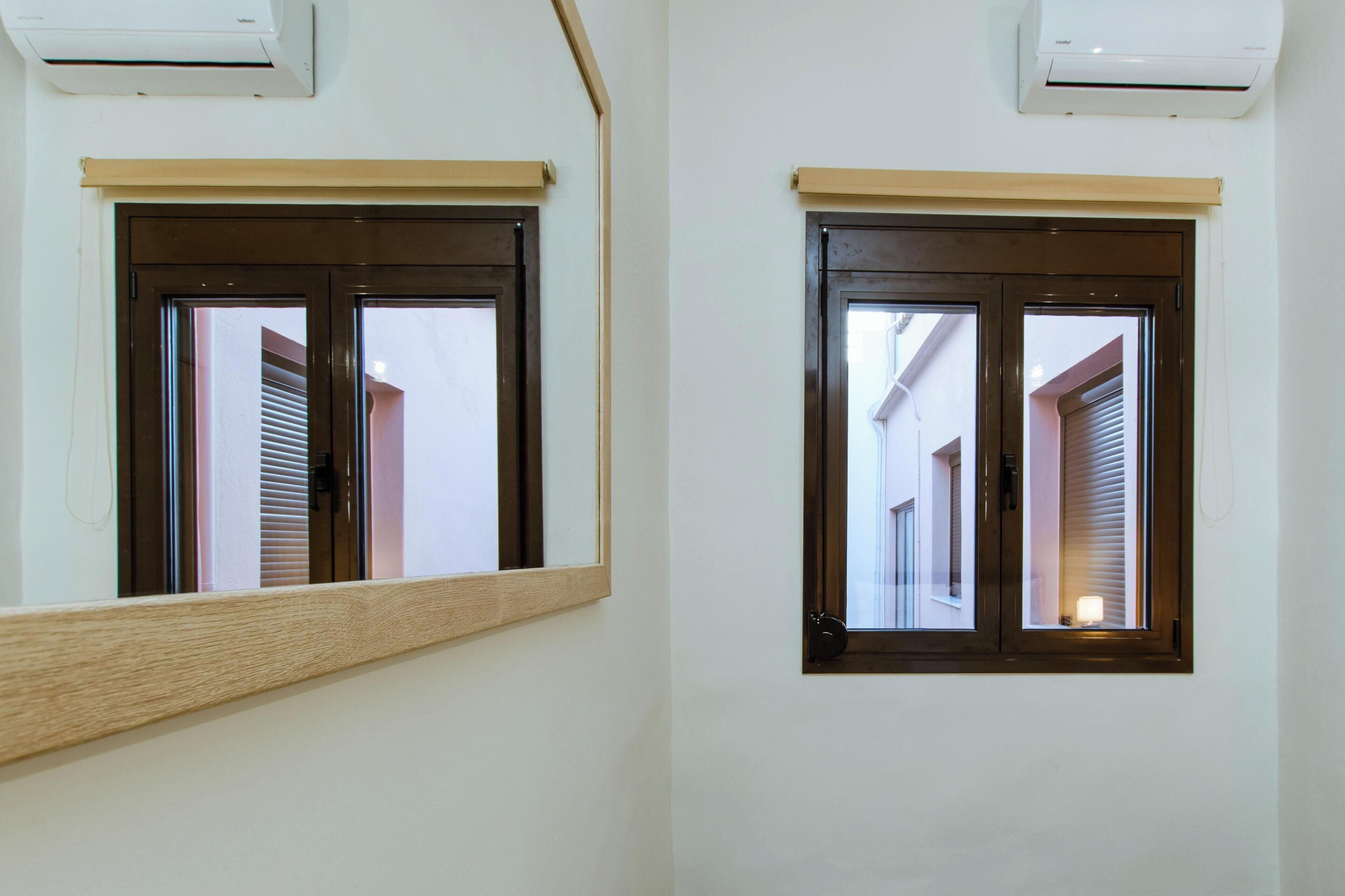 Two windows with wooden frames and blinds, an air conditioning unit above each window, and a wooden ledge in front of the left window.