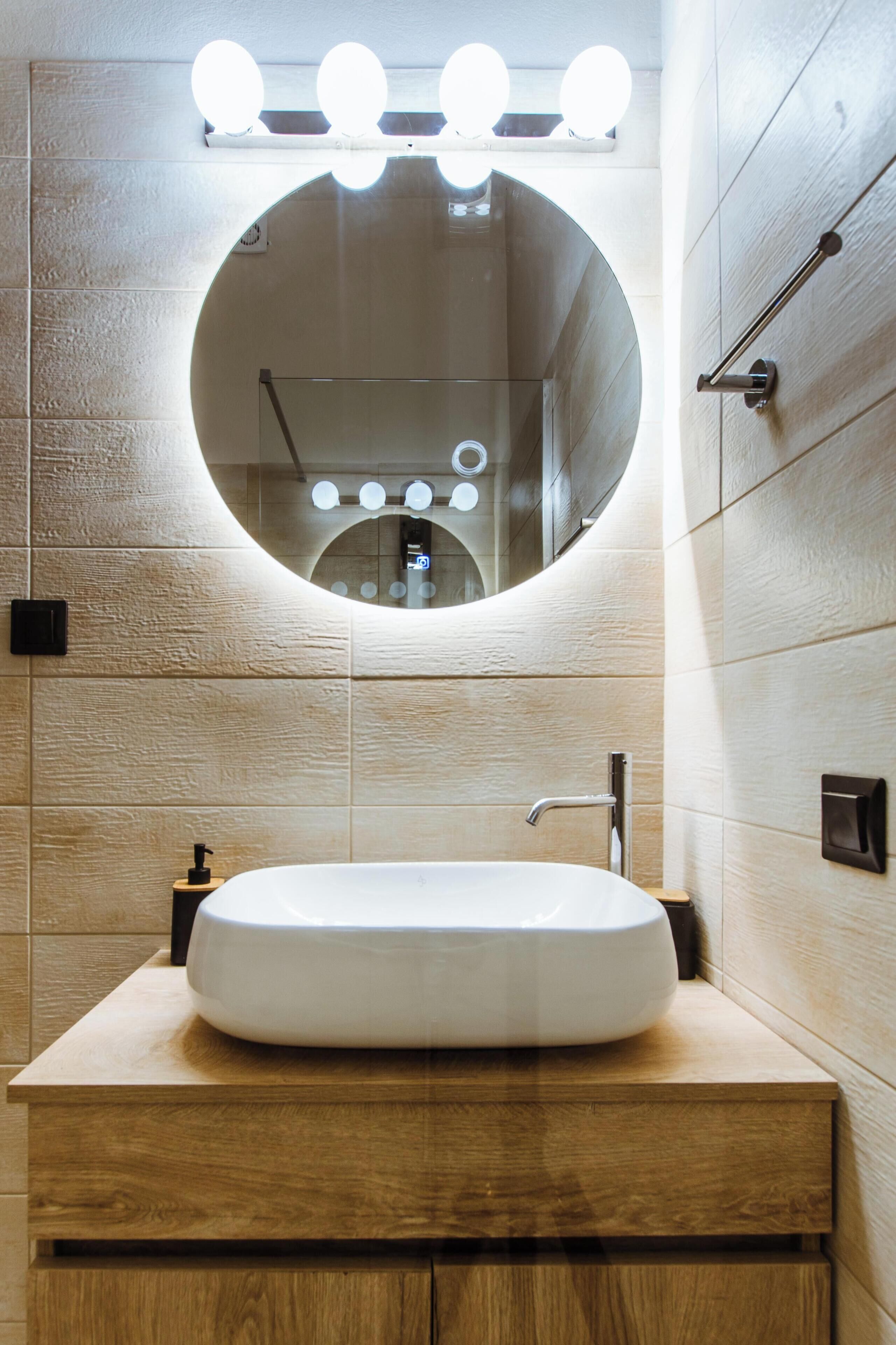 A bathroom with a round mirror, a white sink, and wooden cabinetry.