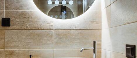 A bathroom with a round mirror, a white sink, and wooden cabinetry.