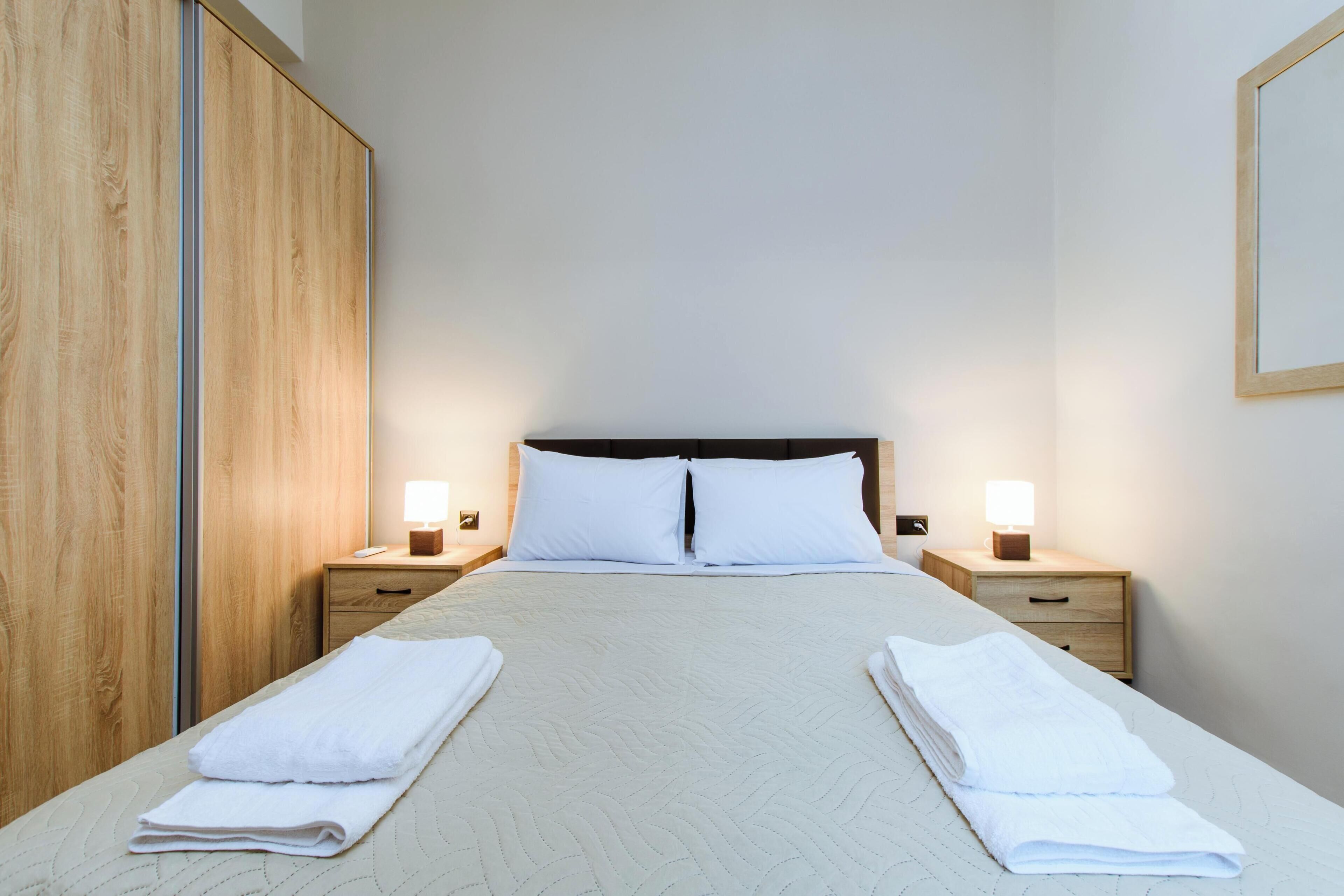 Habitación de hotel con una cama, dos mesitas de noche, un armario de madera y un cuadro colgado en la pared.