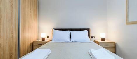 Habitación de hotel con una cama, dos mesitas de noche, un armario de madera y un cuadro colgado en la pared.