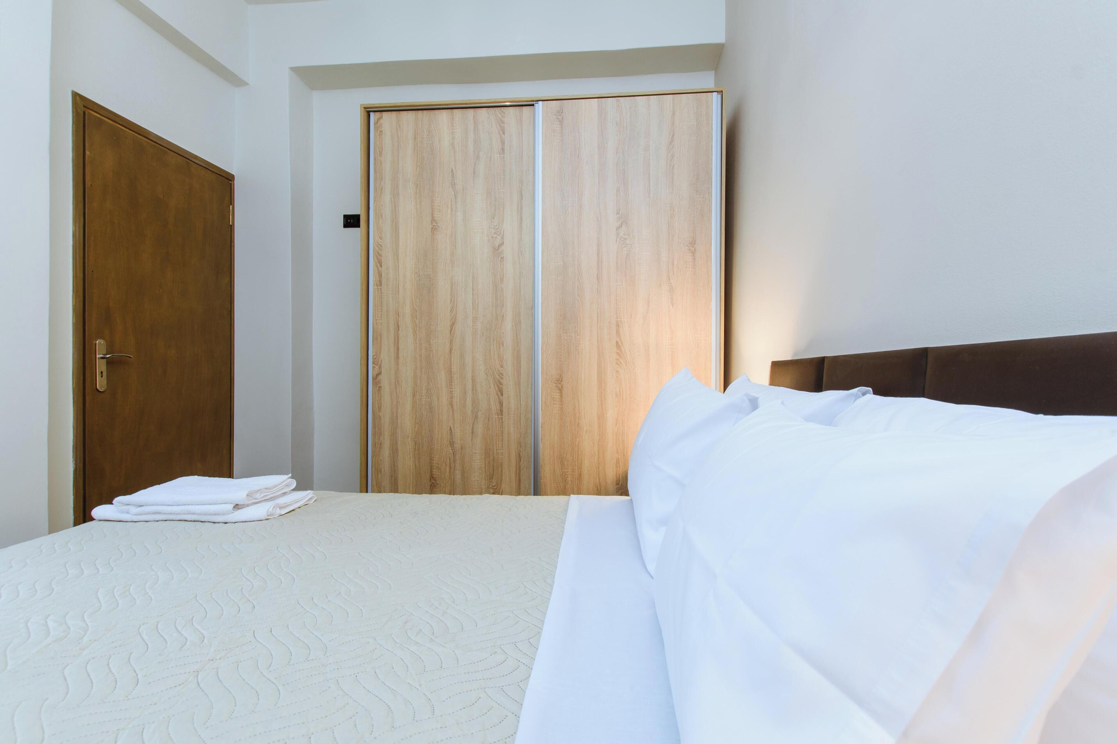 A hotel room with a bed, a wooden wardrobe, and a door.