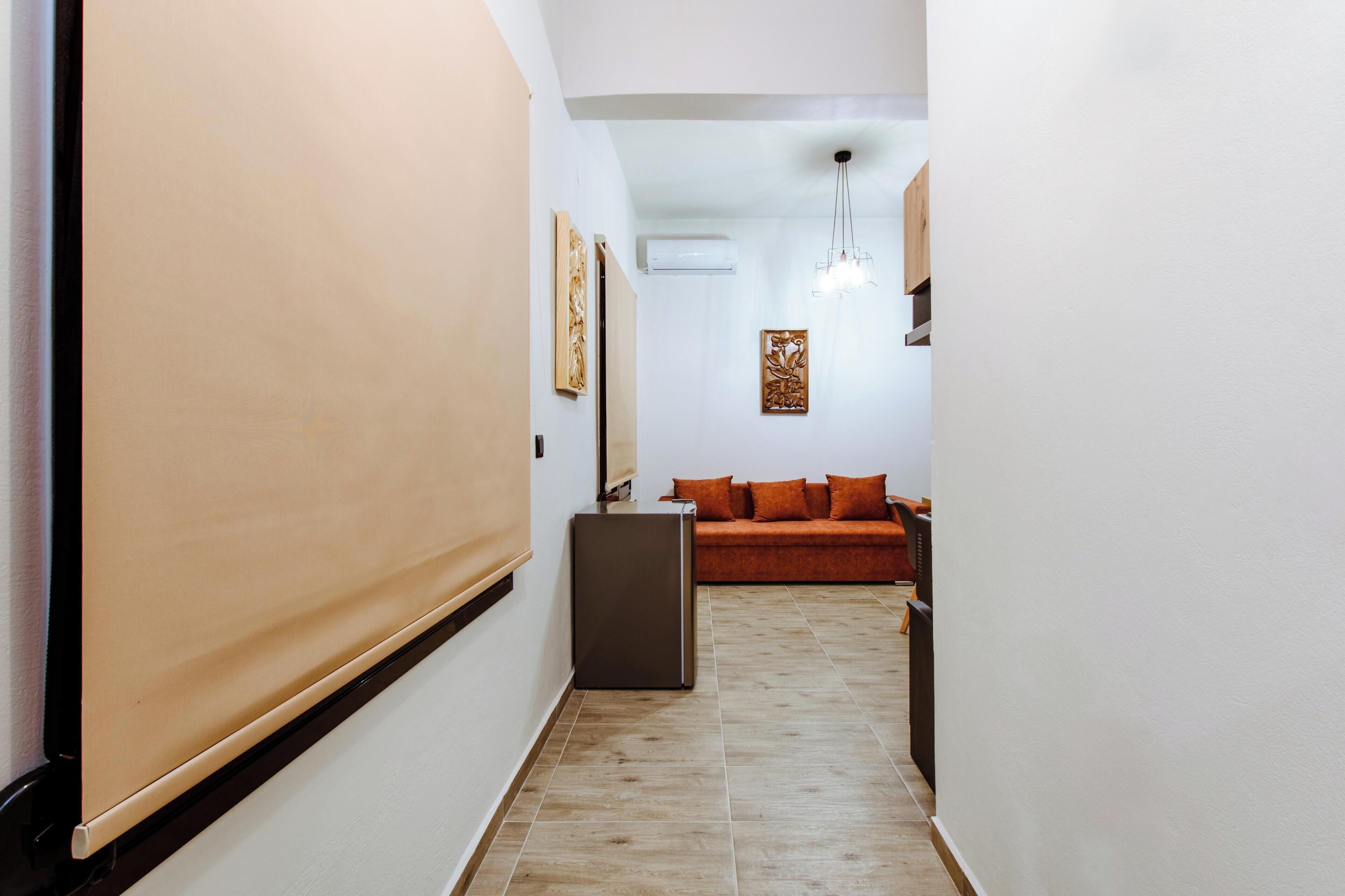 Un couloir avec une porte coulissante, un canapé avec des coussins orange et un luminaire suspendu.