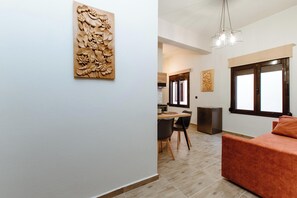 A modern interior with a dining area, a sofa, and a wooden wall carving. - Krinis Home (Chania)