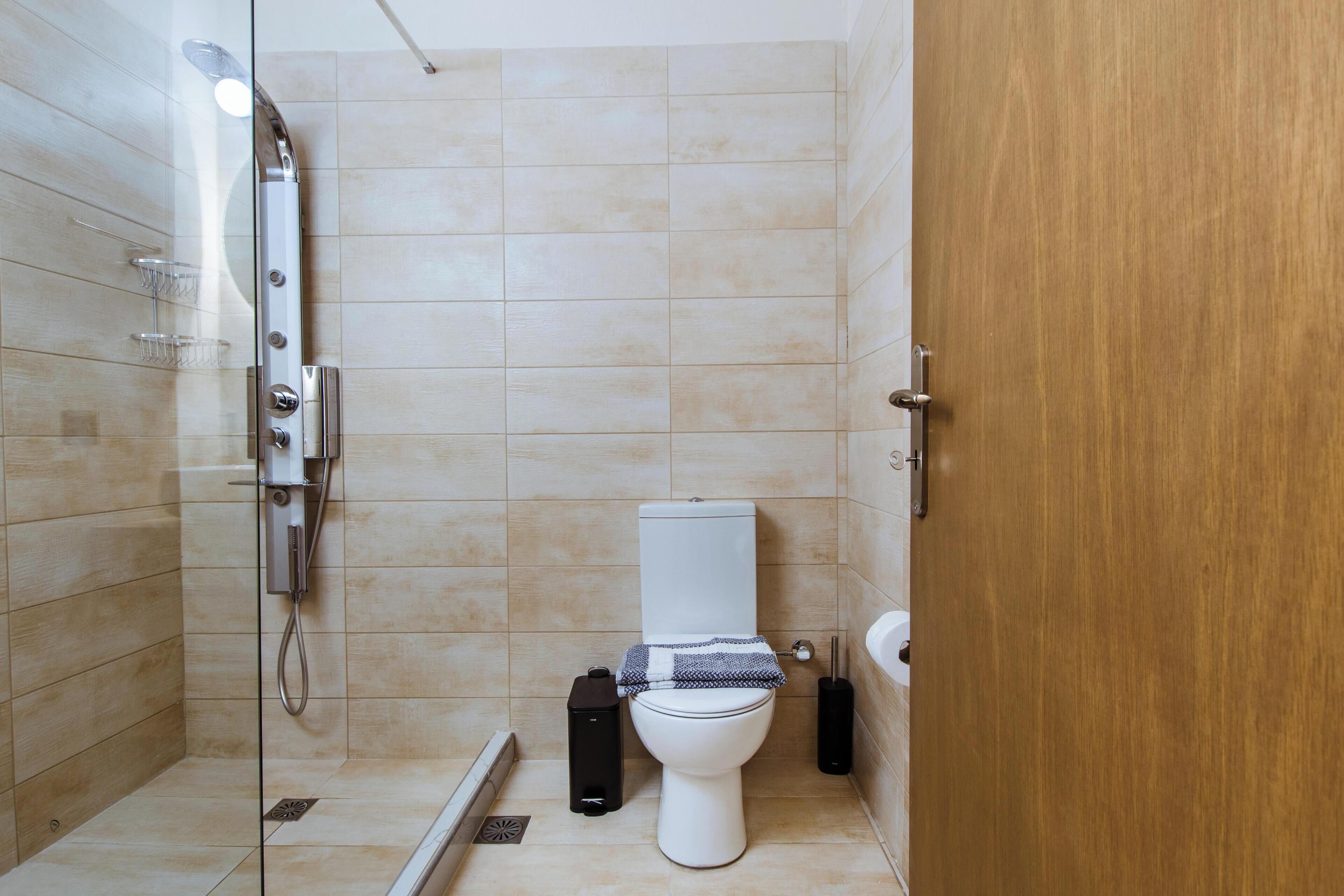 Een moderne badkamer met een douche, toilet en een houten deur.