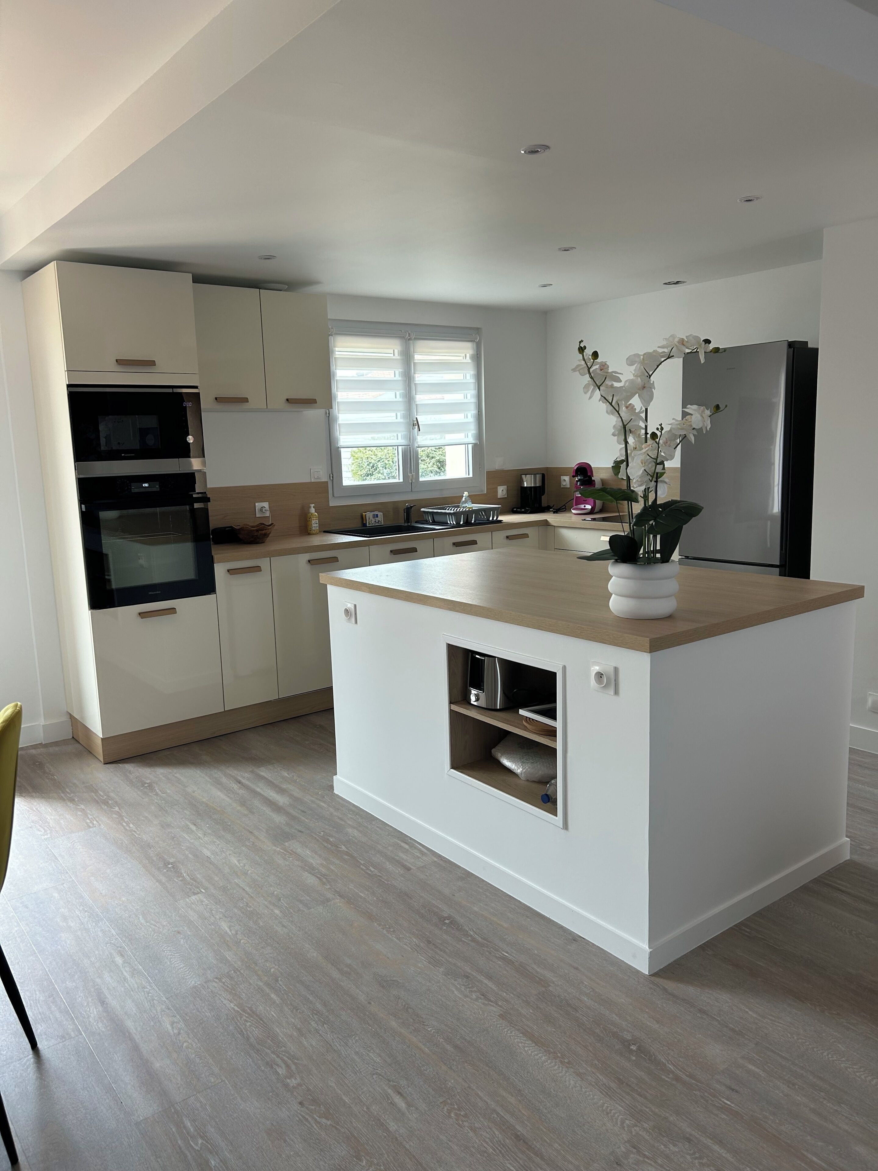 A modern kitchen with white cabinetry, a wooden island, built-in appliances, and a window providing natural light.