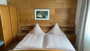 A bedroom with a wooden headboard, a bed with two pillows, a nightstand, a bedside table, and a framed picture on the wall.