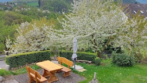 A garden with a wooden table and benches, surrounded by blooming trees and a stone pathway.
