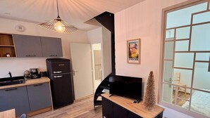 Een moderne keuken met een zwarte koelkast, een houten eettafel en een televisie op een zwart tv-meubel.