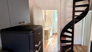 Een compacte keuken met een ingebouwde wasmachine, een zwart opbergmeubel en een spiltrap.