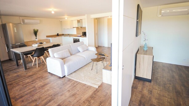 A modern apartment with a dining area, a sofa, a small table, and a kitchen in the background.