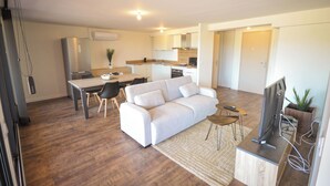 A modern apartment with a dining area, sofa, TV, and kitchen.