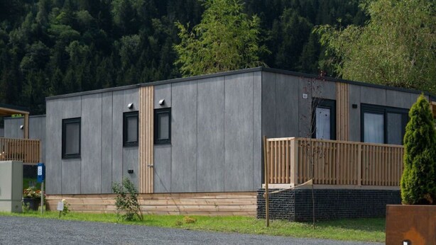 A modern, single-story building with a flat roof, a small porch, and a gravel driveway. - Wulfenia Waterfront 6 (Ossiach)