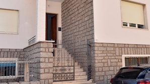 A building with a stone facade, a set of stairs leading to a door, and a parked car. - My Holiday Olbia Rooms & Lounge Room 4 by Rentbeat (Olbia)