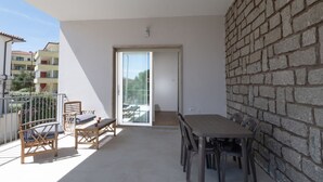 A balcony with a table and chairs, a sliding glass door, and a brick wall. - My Holiday Olbia Rooms & Lounge Room 4 by Rentbeat (Olbia)