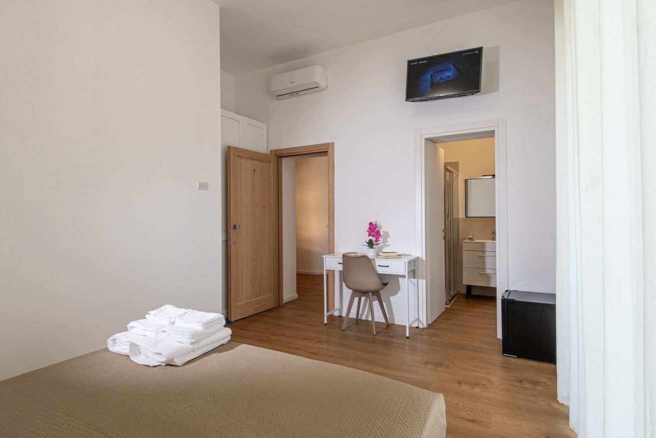 A hotel room with a bed, a desk, a chair, a TV, and a small kitchenette.