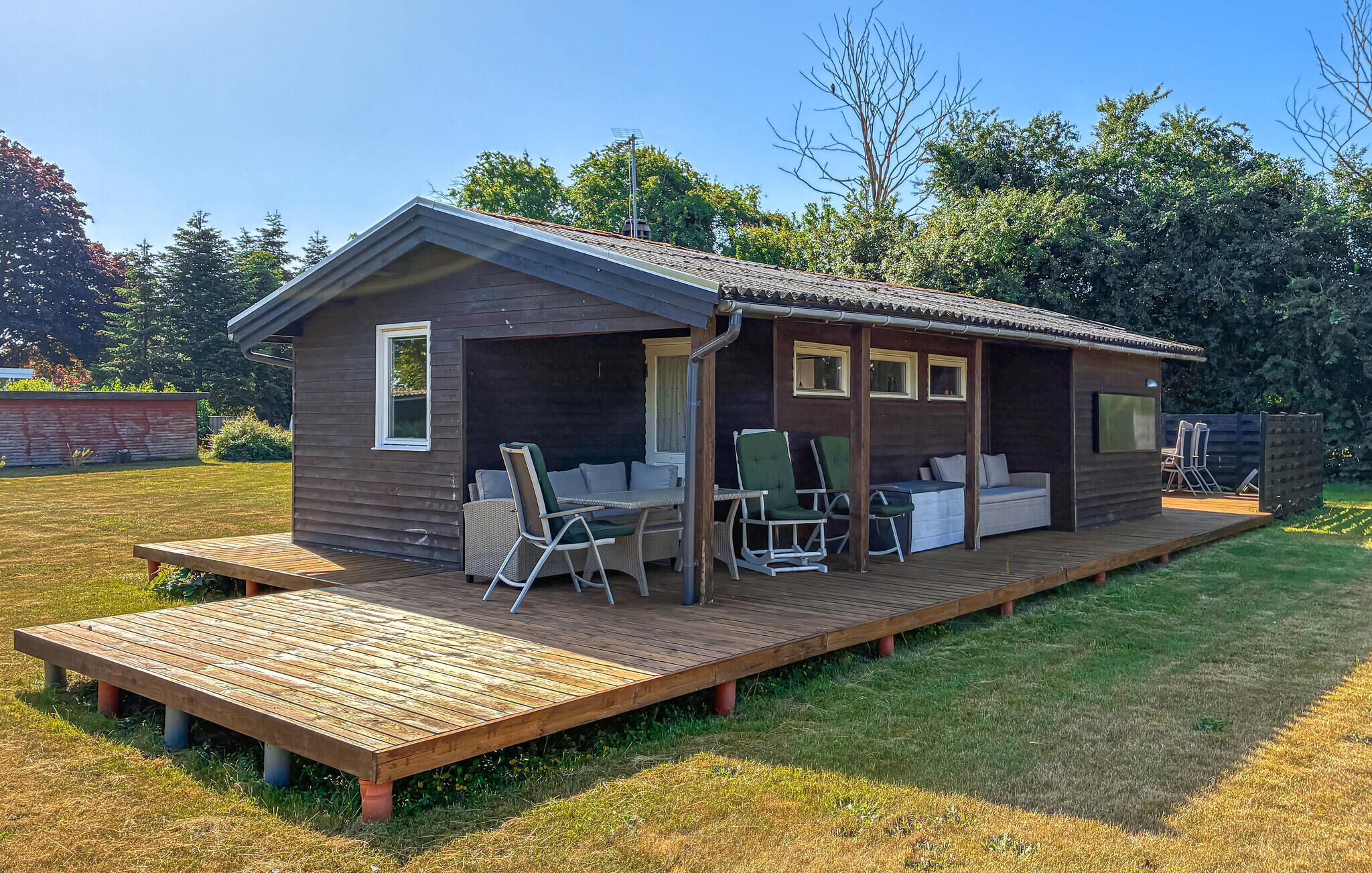 A wooden cabin with a deck, outdoor seating, and a TV.