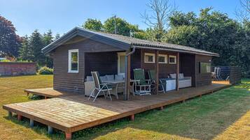 A wooden cabin with a deck, outdoor seating, and a TV.