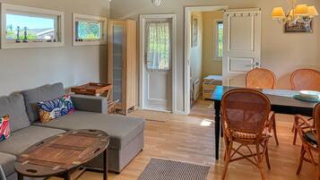 A living room with a sofa, a coffee table, wicker chairs, a dining table, and a view through a door.