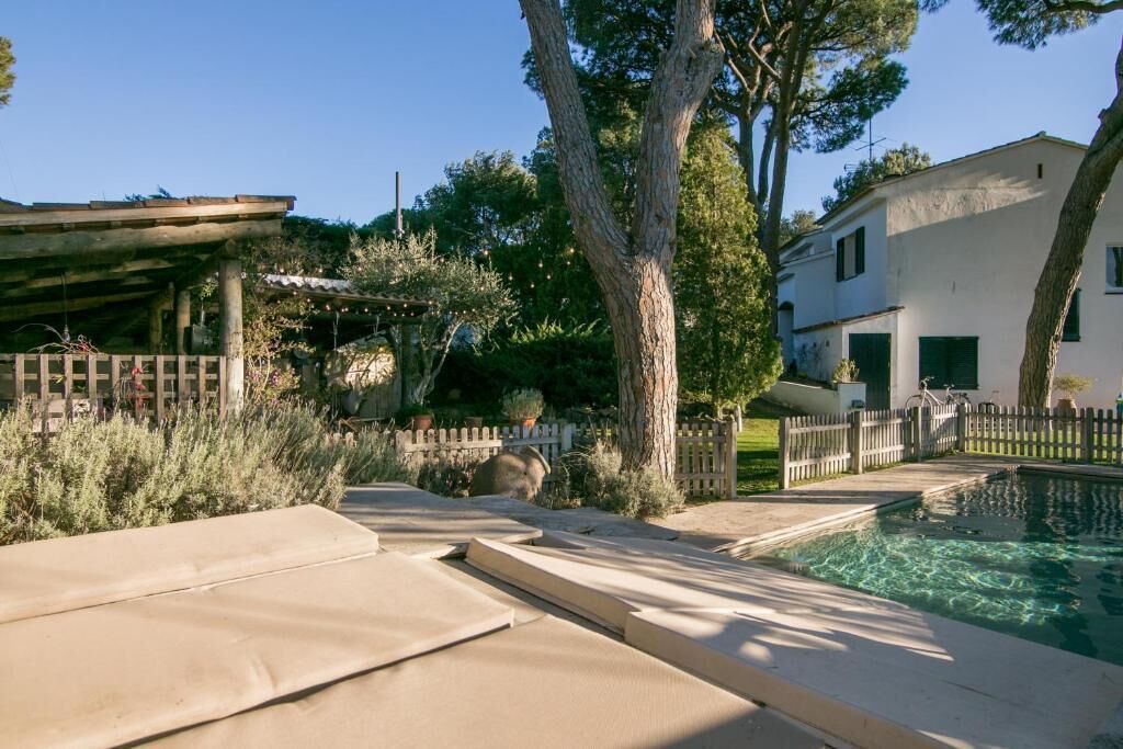 Un espace piscine agrémenté d’une pergola, d’arbres et d’un bâtiment blanc.