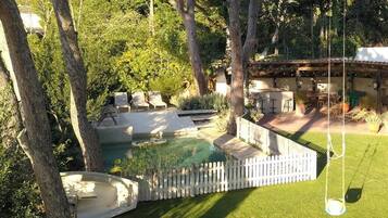 A backyard with a swimming pool, lounge chairs, a deck, and a pergola.