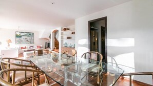 A modern dining area with a glass table and wicker chairs, a white sofa, and a staircase leading to an upper level. - VILLA CANADELL (Palafrugell)
