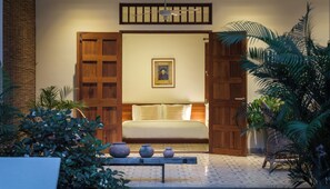 A room with a bed, wooden doors, a ceiling fan, a framed picture, and potted plants.